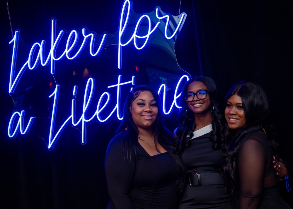 3 girls in front of Laker for a Lifetime neon sign